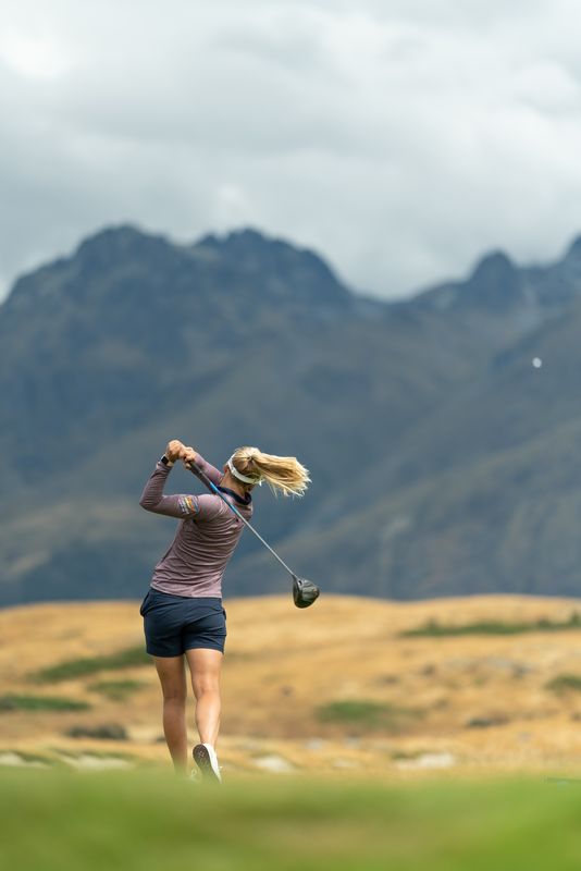 Pernilla Lindberg follows through on a drive, with mountains rising behind the course
